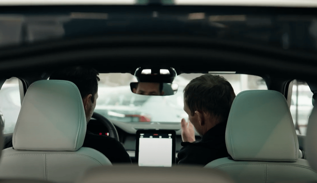 Interior view of Polestar car with two people seated in front, central touchscreen visible, exterior cars in background.