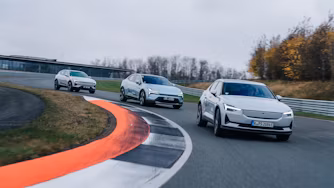 Three Polestar cars driving on a curved racetrack with grass and trees in the background.