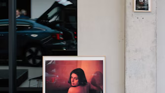 Polestar car with open trunk reflected in glass, framed artwork on concrete wall.