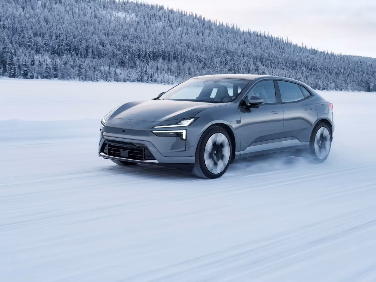 Polestar car driving on snow-covered road with forest in background.