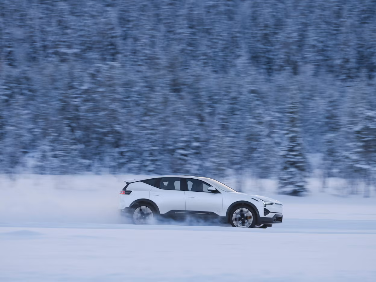 Polestar car driving on snow-covered terrain with blurred forest in the background.