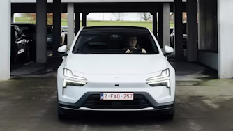 Front view of a white Polestar car parked under a concrete structure with other vehicles in the background.