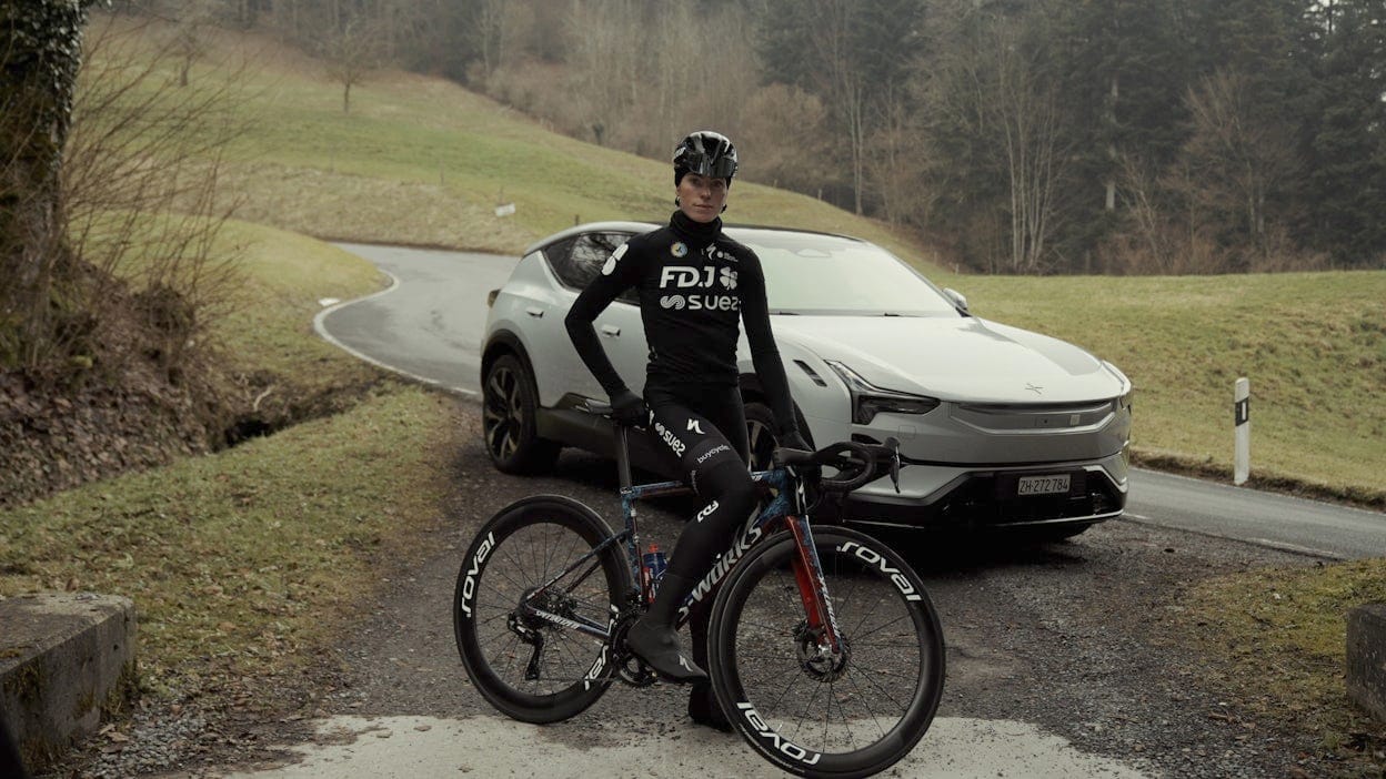Demi Vollering met fiets in de hand, op de achtergrond staat een Polestar 3