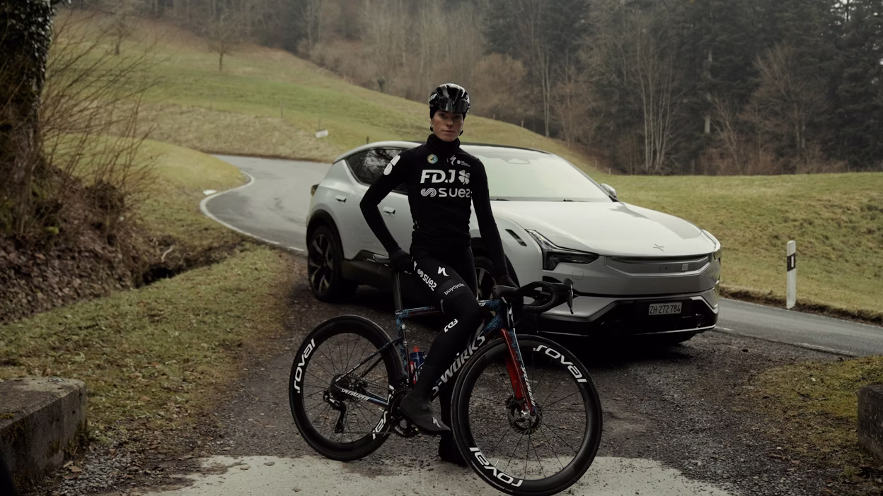 Demi Vollering met fiets in de hand, op de achtergrond staat een Polestar 3