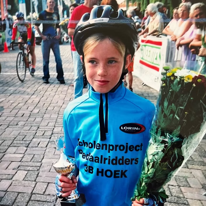 Demi Vollering als kind met bloemen in haar handen bij de finish van een fietswedstrijd.