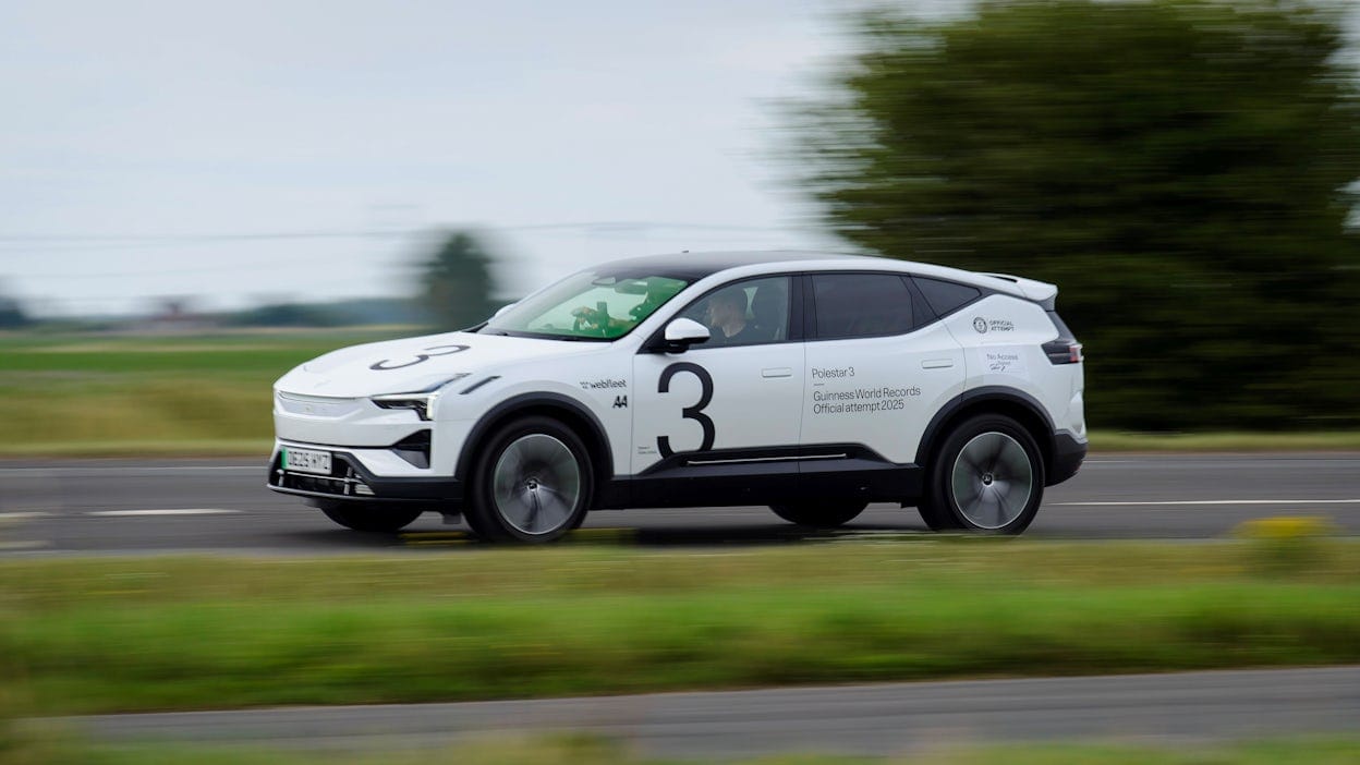 Vit Polestar 3 kör på asfalterad väg med träd i bakgrunden