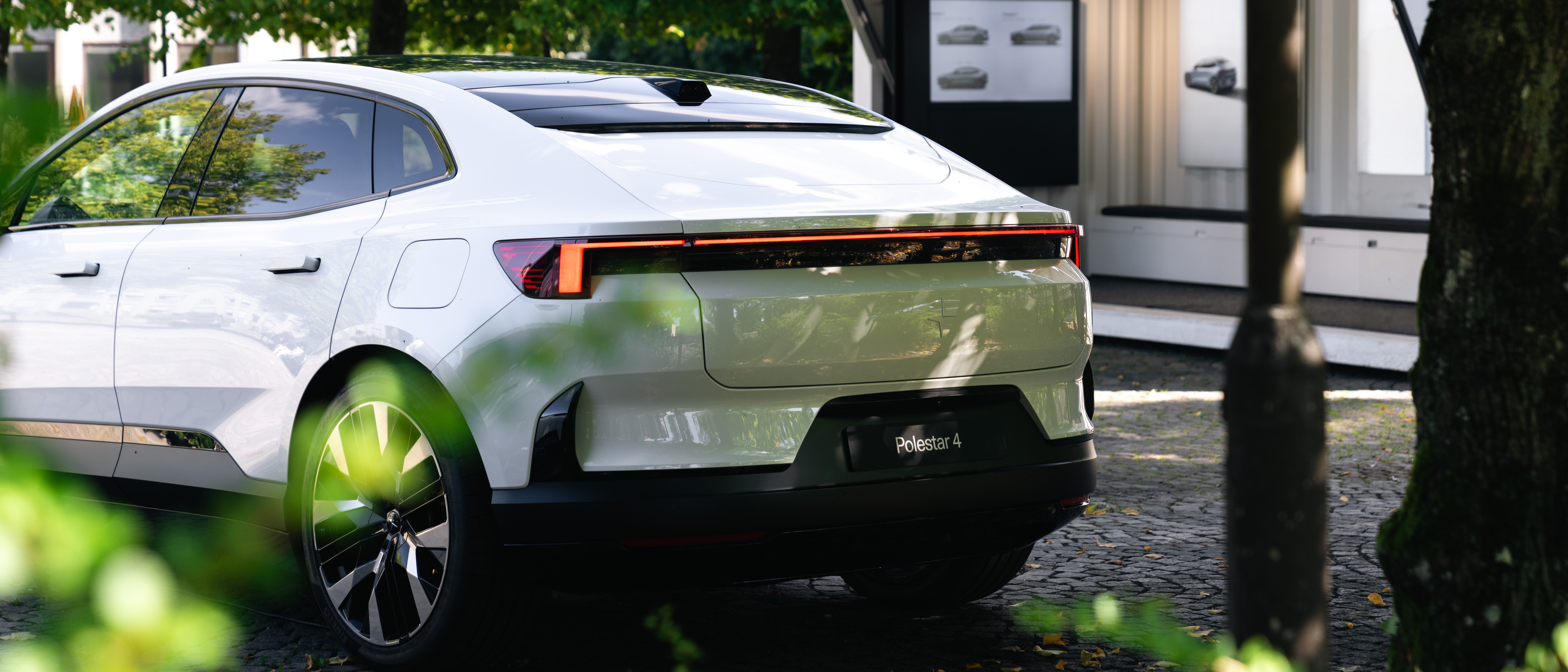 Vit Polestar 4 med eventcontainer i bakgrunden och gröna löv i förgrudnen