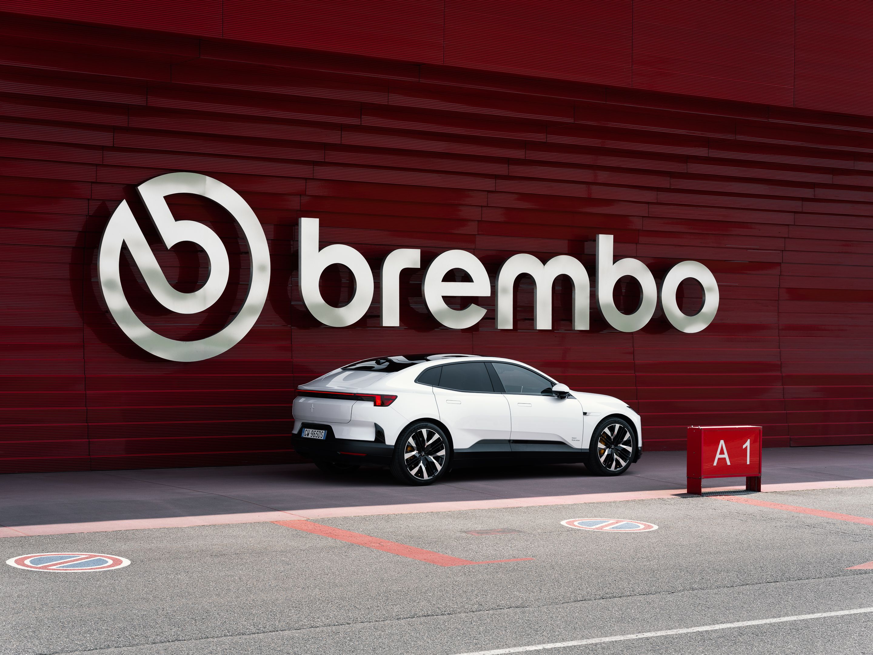 Polestar 4 in front of large red wall with silver Brembo logo