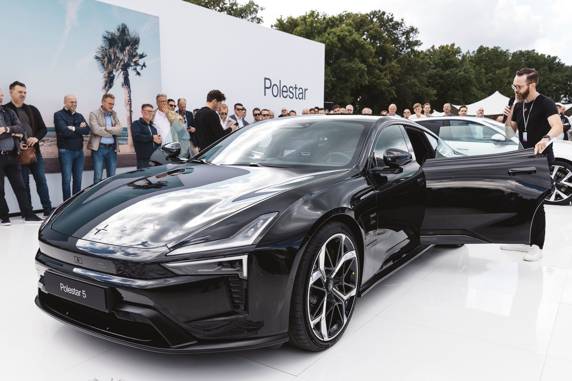 Polestar 5 staat op een wit platform met mensen eromheen.