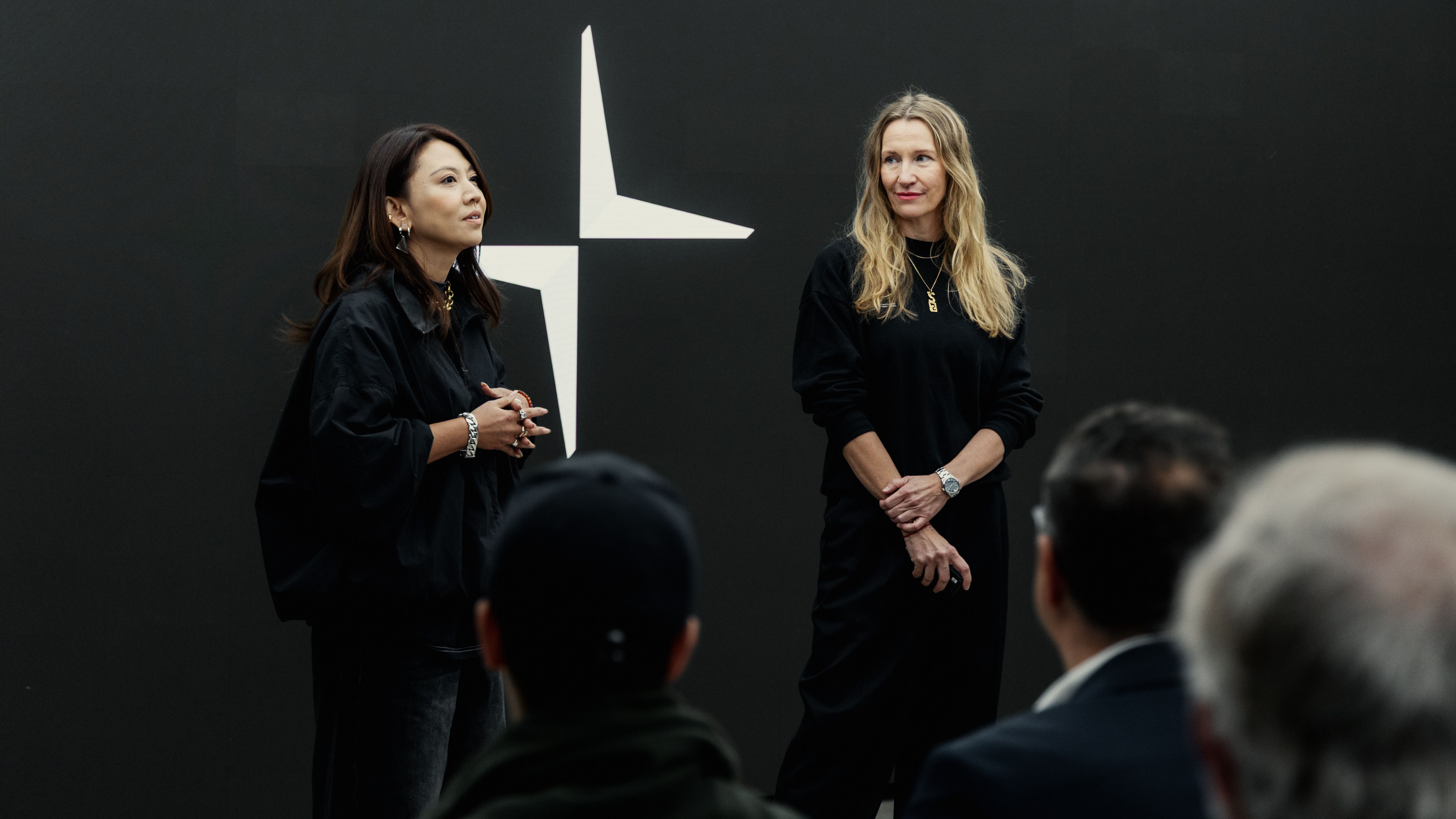 Two pesenters talking in front of a crowd, black backdrop with the Polestar logo