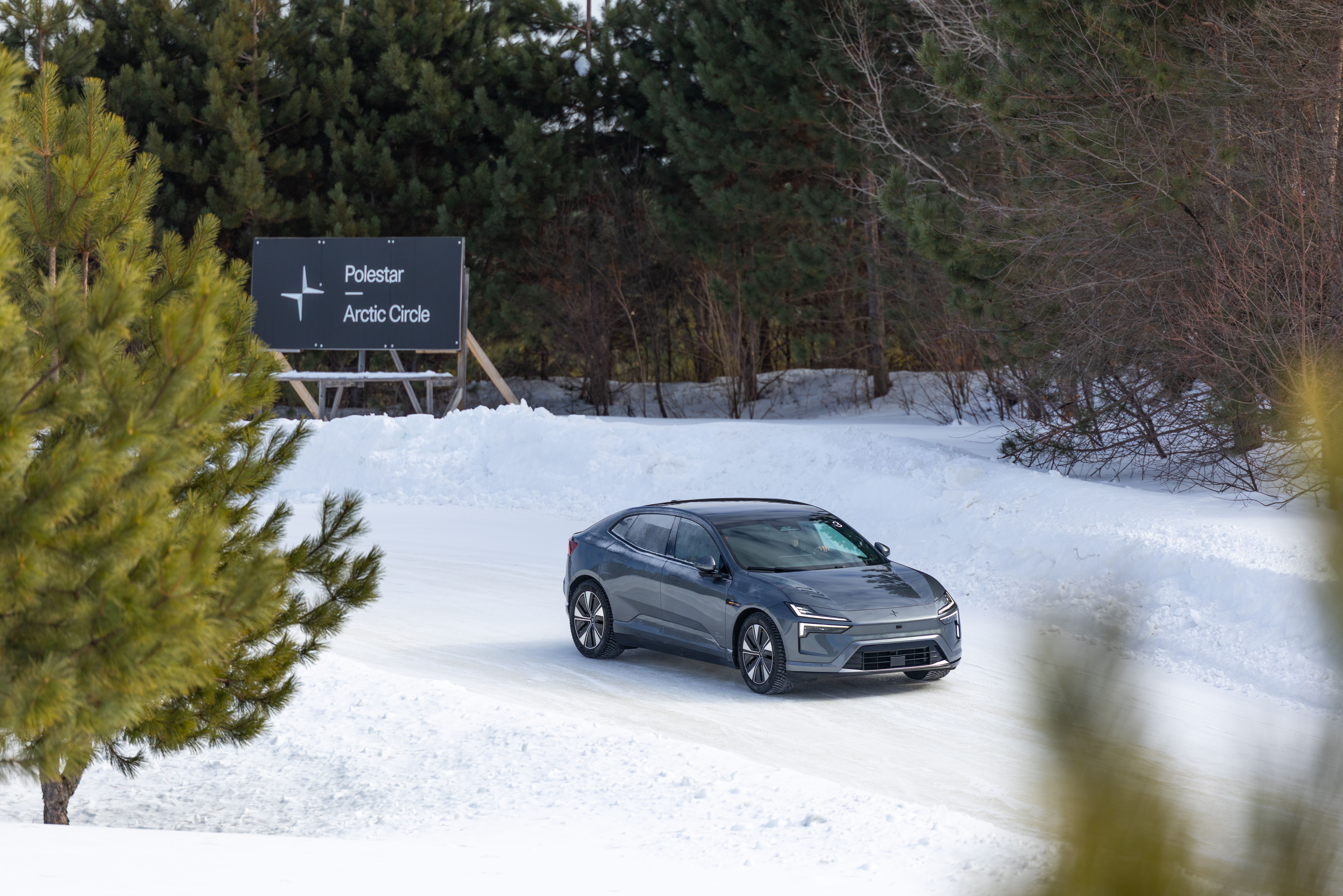 Polestar 4 on snow road near sign reading Polestar Arctic Circle, trees in background