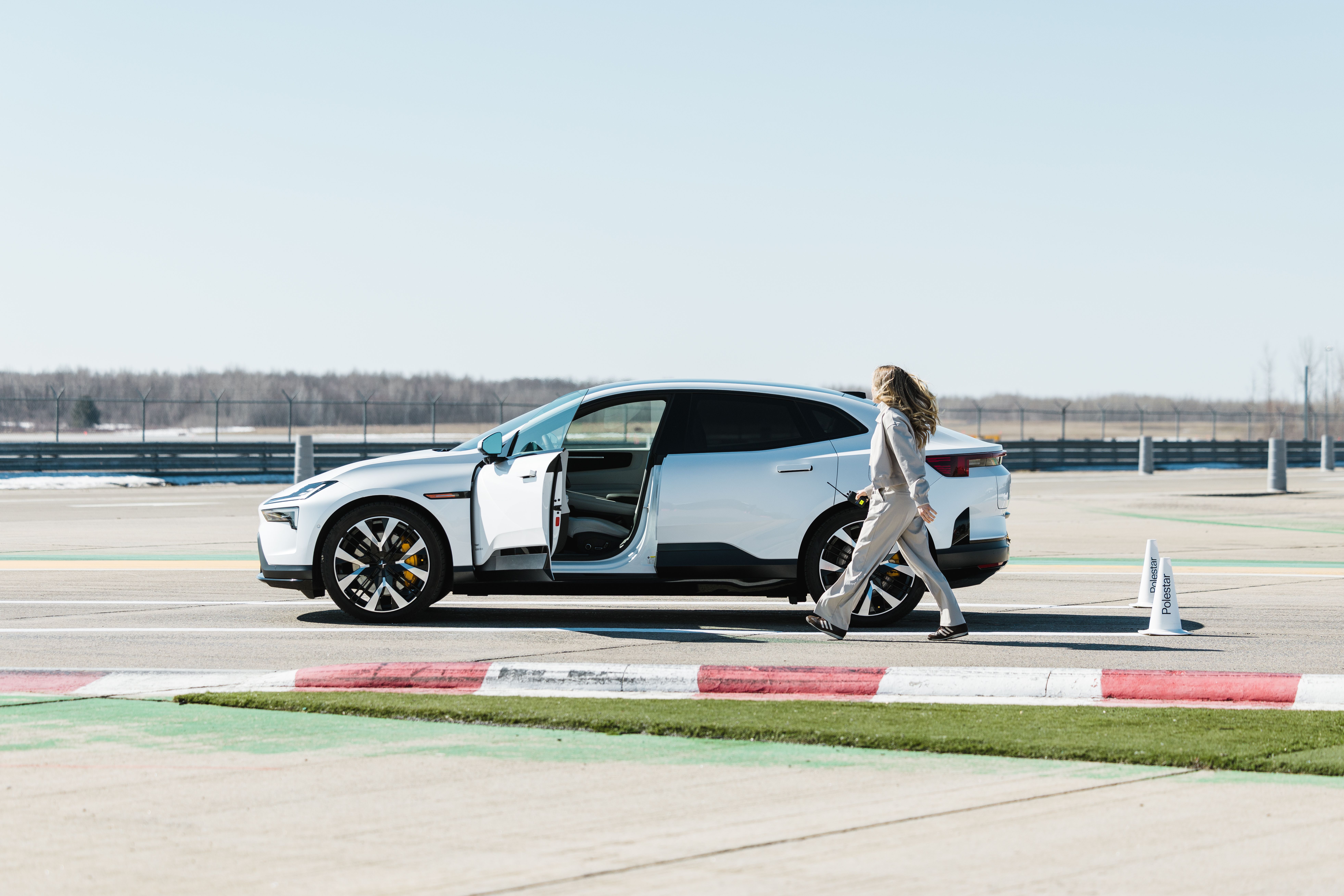 Polestar 4 Coupé with open driver door on a racetrack, person walking beside it