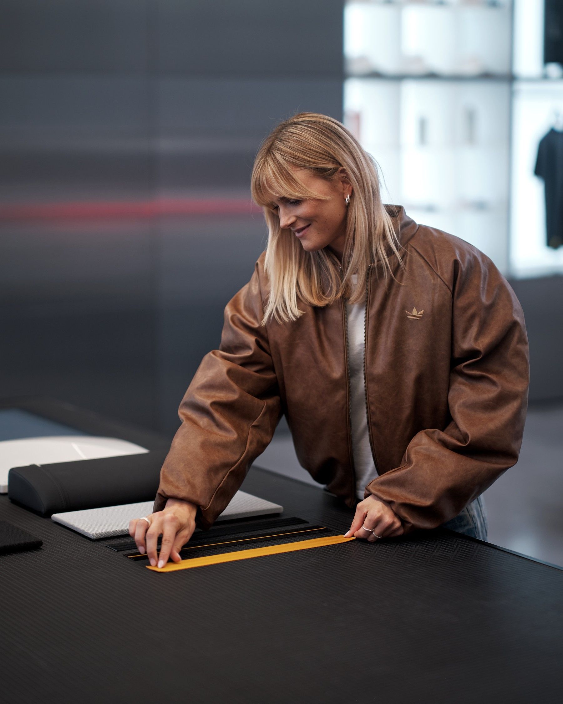 Blond tjej i brun jacka står och tittar på interiörprover till bil vid ett svart bord