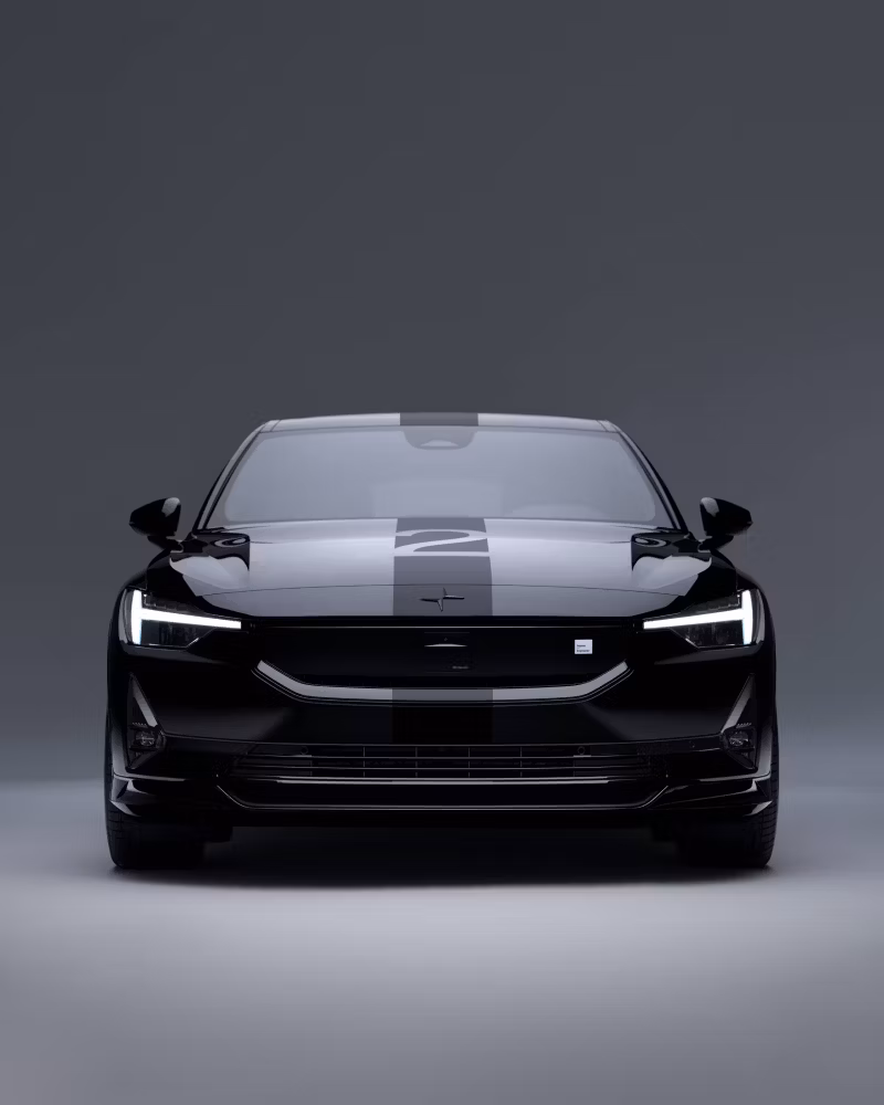 Front view of Polestar car with headlights on, black exterior, and stripe design on hood against gray background.