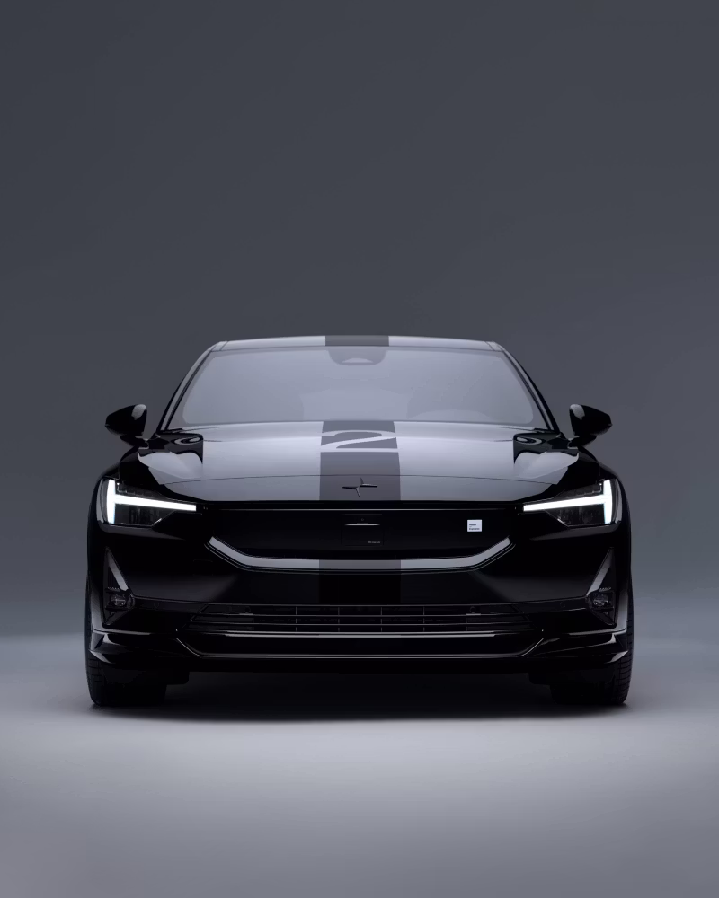 Front view of Polestar car with headlights on, black exterior, and stripe design on hood against gray background.