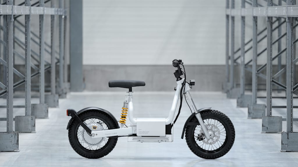 A white/gray Cake Makka bike parked in a gray room with concrete floors surrounded by metal beams in rows