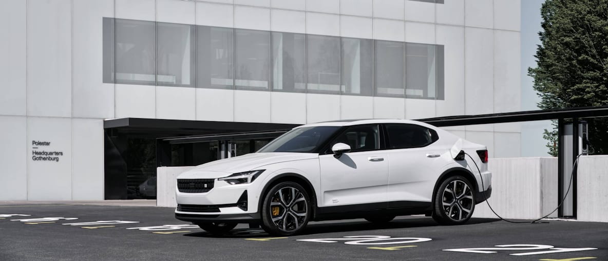 Side view of white Polestar charging infront of glass facade building