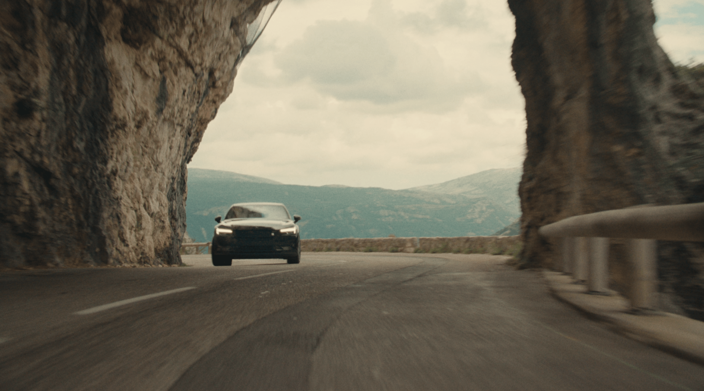 Polestar 2 driving through narrow streets and on a motorway by the side of a mountain.