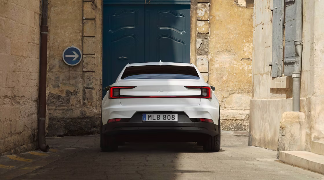 Polestar 2 facing a blue door while standing in an antiquated alleyway half under the shadows.