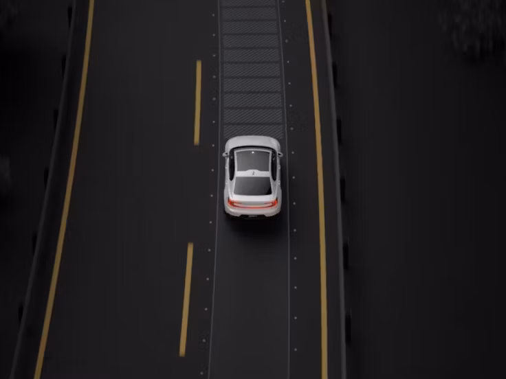 Een bovenaanzicht van de witte Polestar 2 rijdend op een snelweg met gele rijstrookmarkeringen