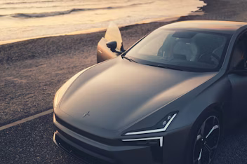 Voorkant van de Polestar 5 op de weg naast een strand.