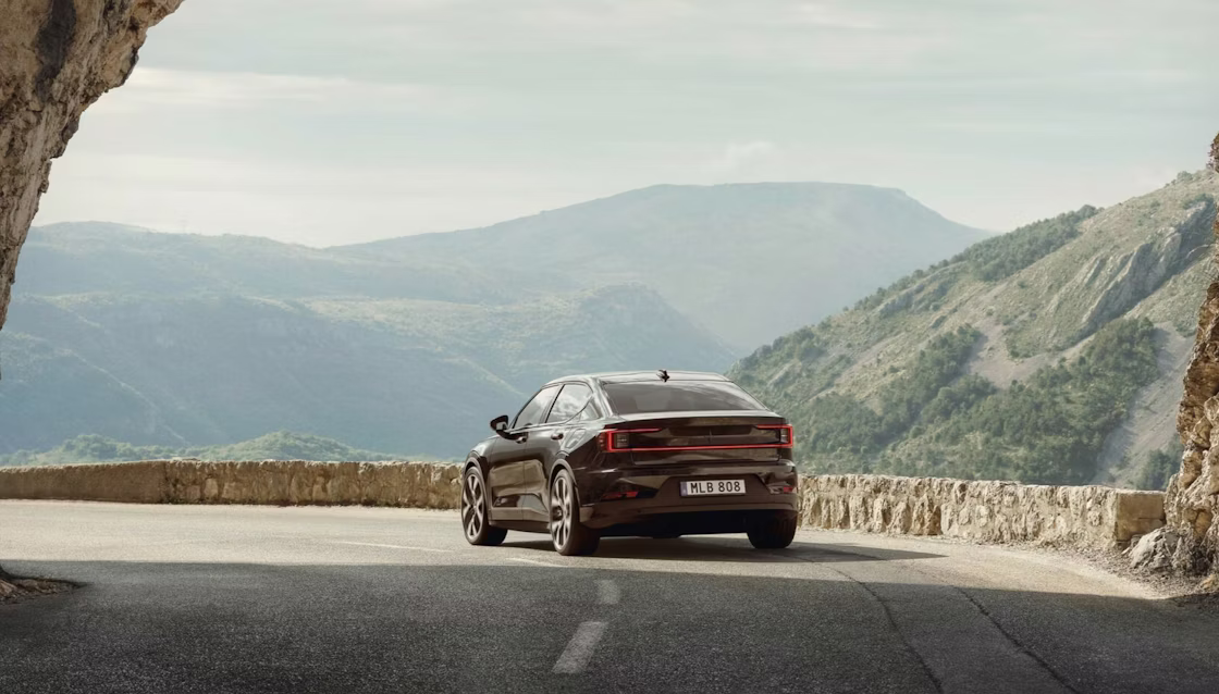 Polestar 2 driving away from an arched rock formation on a highway in a hilly area.