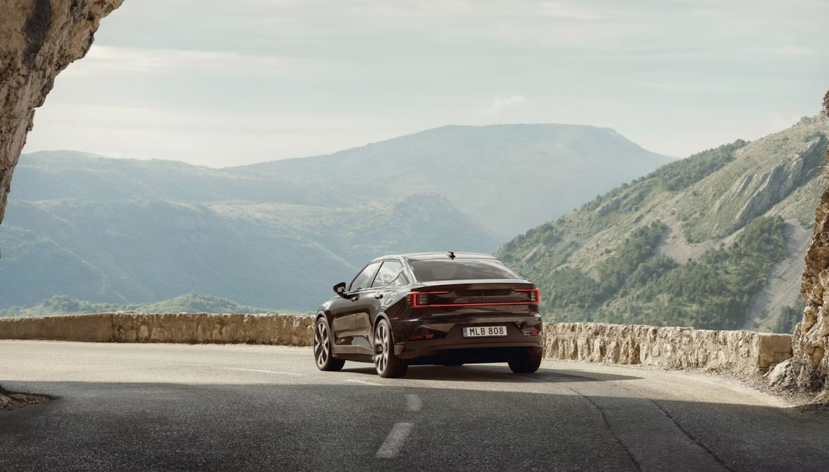 Polestar 2 rijdt weg van een gewelfde rotsformatie op een snelweg in een heuvelachtig gebied.