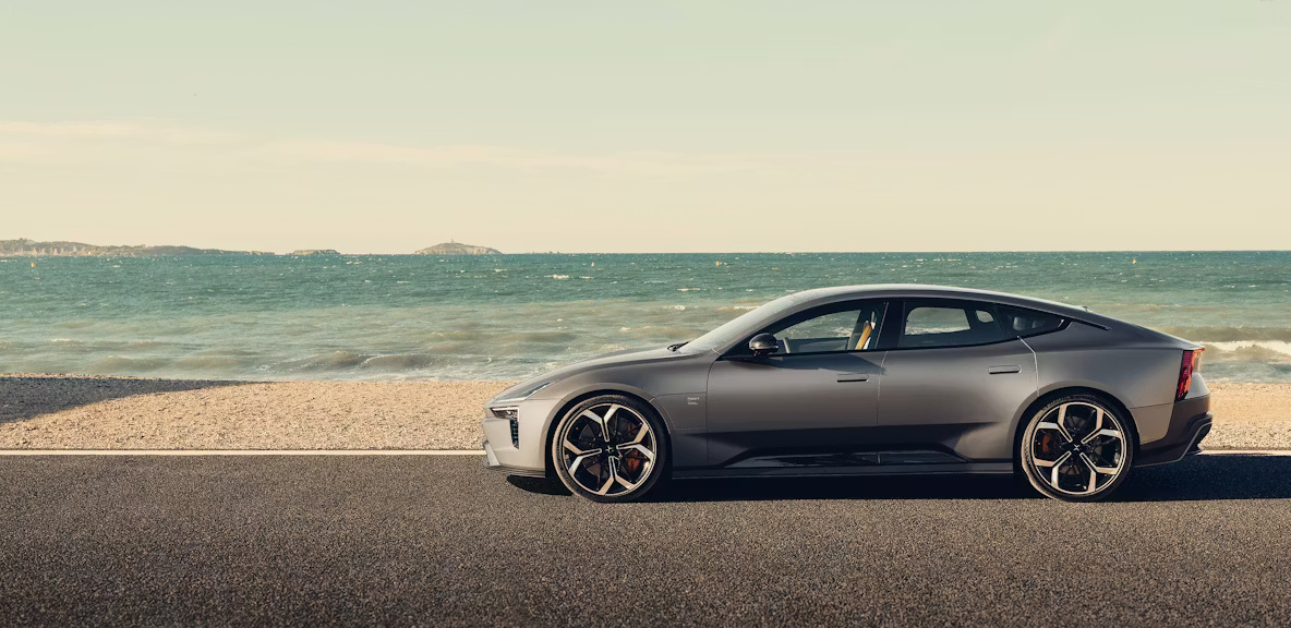 Polestar 5 parked on a road near a beach with ocean and distant islands visible under a clear sky.