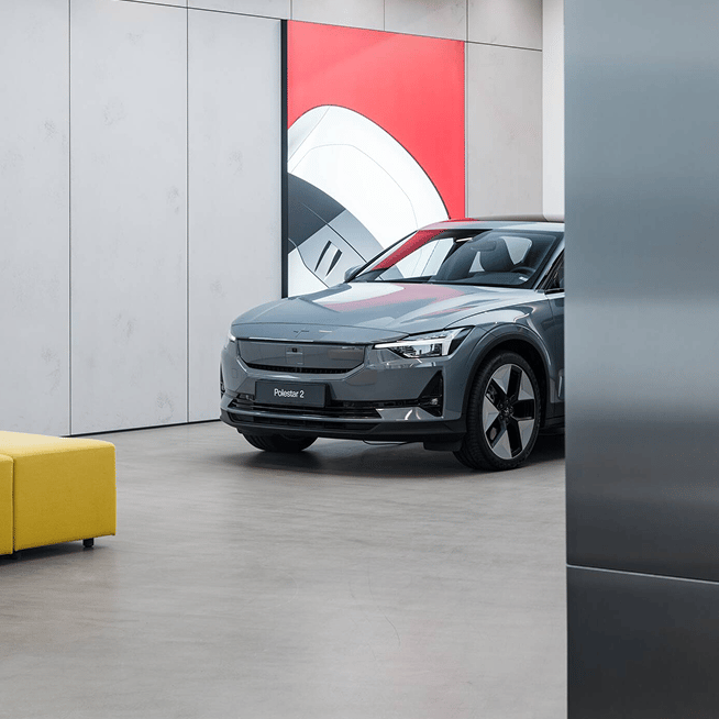 Polestar 2 car parked indoors in a Space near a yellow sofa and a wall with red and white artwork.