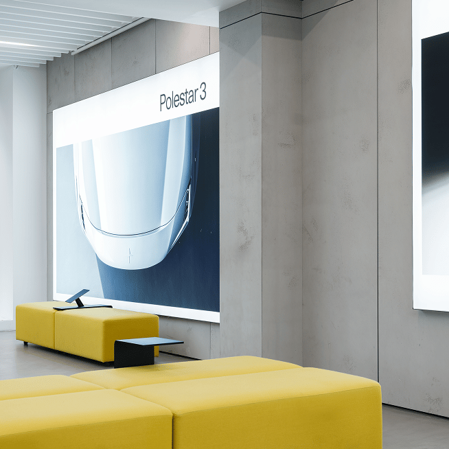 Interior with yellow seating, wall display showing front view of Polestar 3 car.