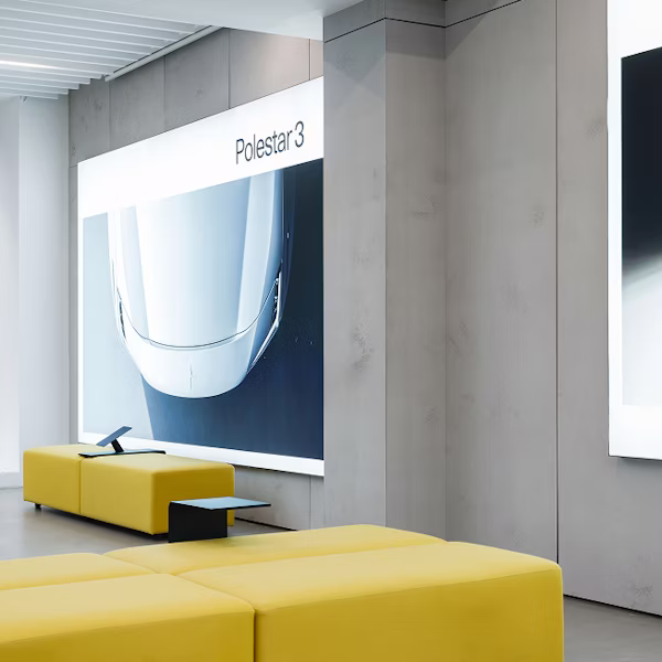 Interior with yellow seating, wall display showing front view of Polestar 3 car.