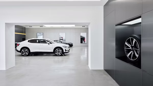 White Polestar 2 car in showroom with another car in background and a wheel displayed in a wall compartment.