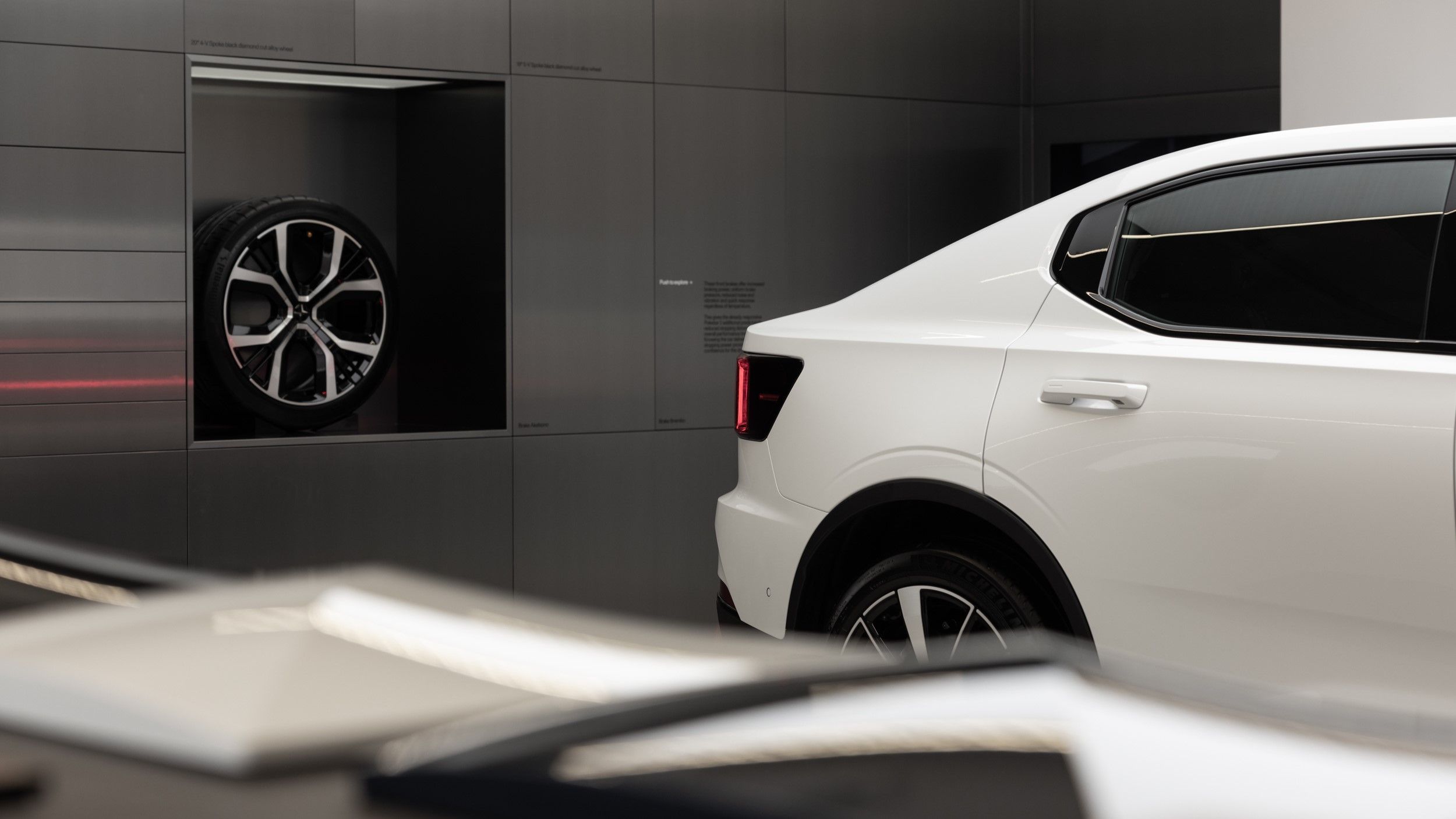 Vit Polestar 2 med lådvägg i bakgrunden i rostfritt stål