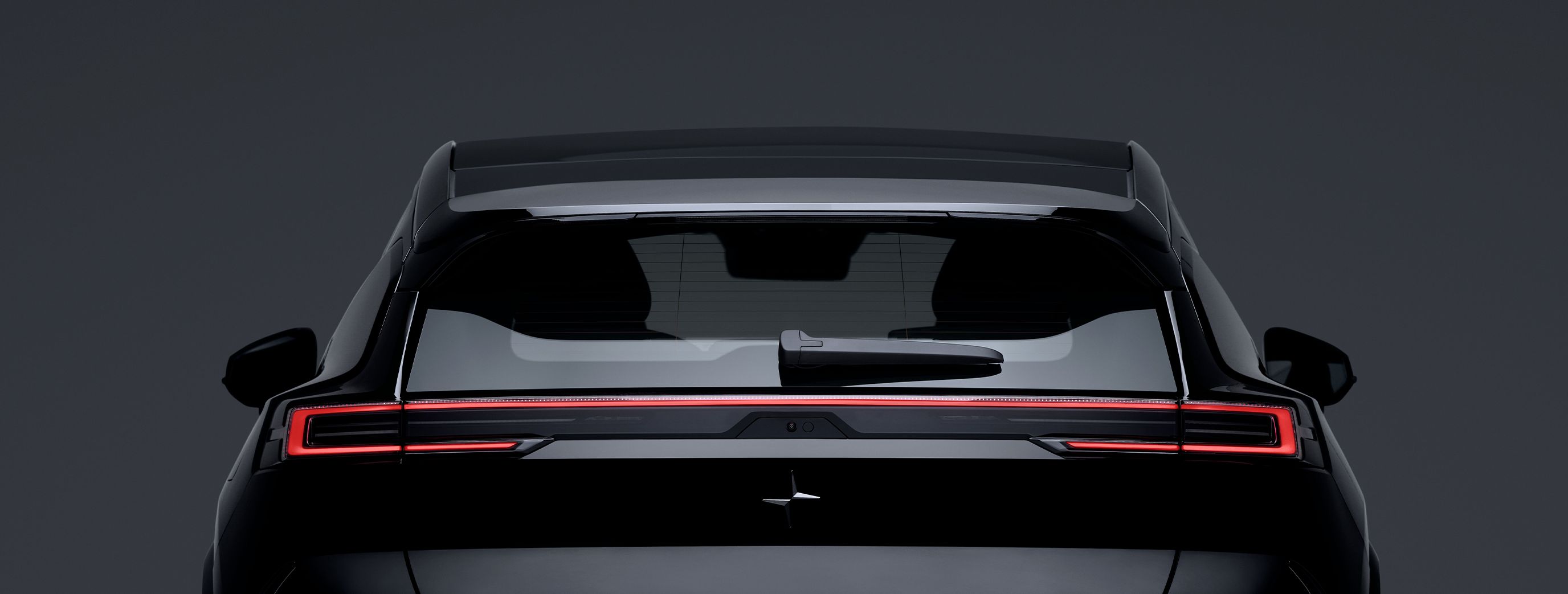 Rear view of Polestar 3 with illuminated taillights and rear windshield wiper against a dark background.