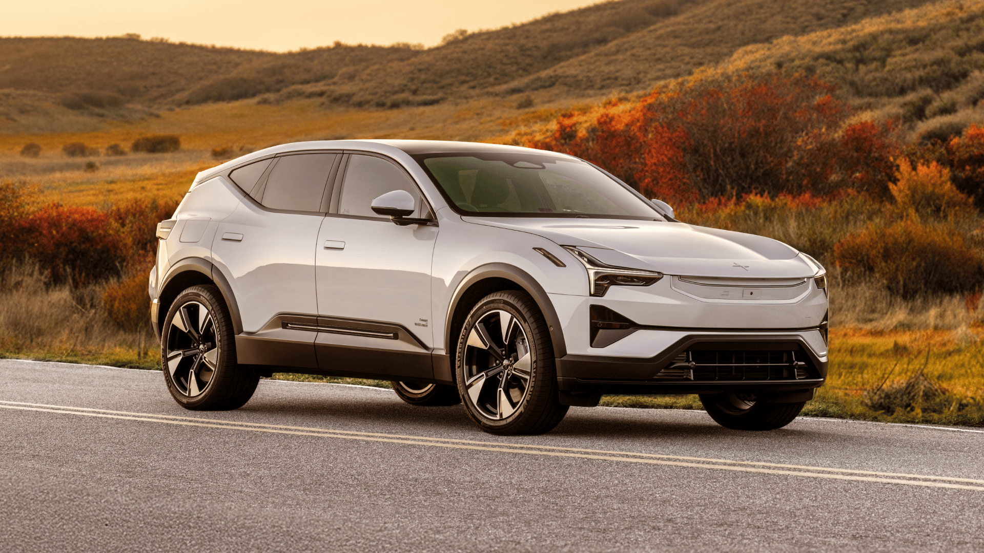 White Polestar 3 driving on a scenic road with autumn foliage.