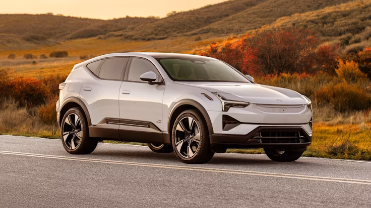 White Polestar 3 driving on a scenic road with autumn foliage.