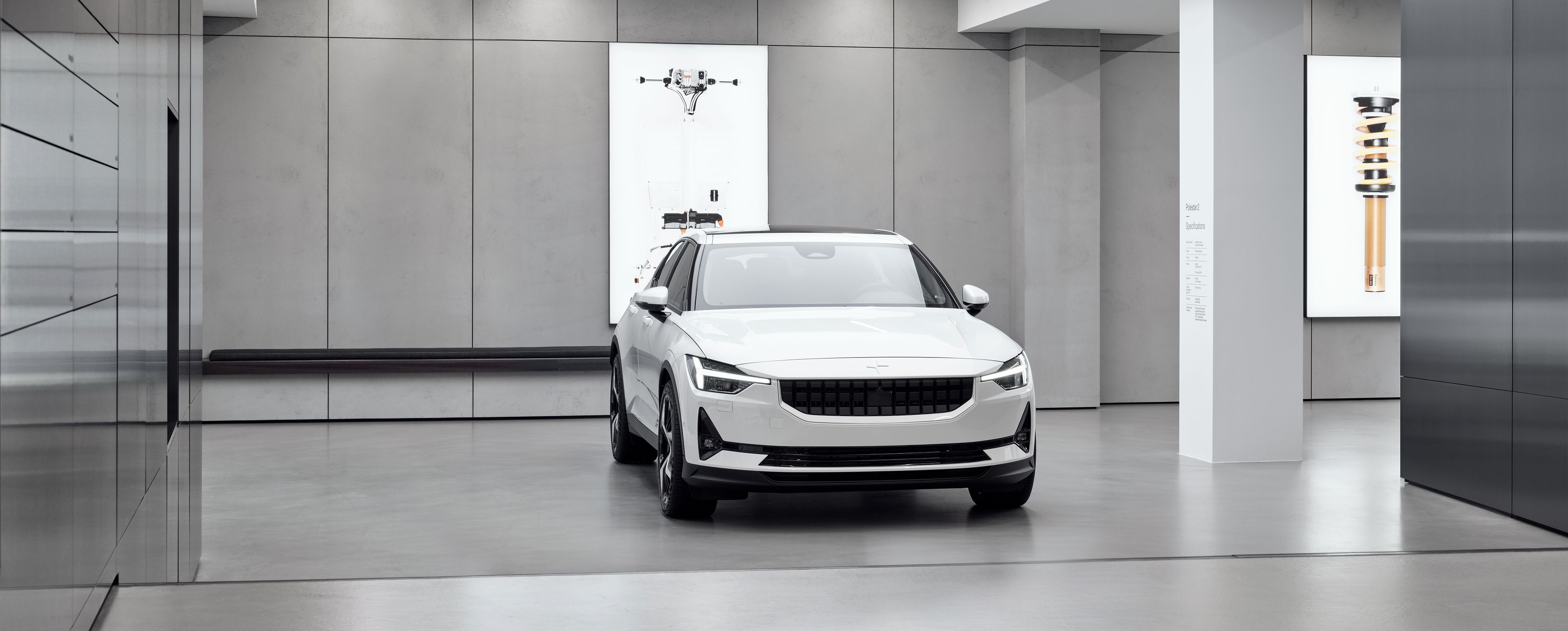 Polestar 2 in a showroom with gray walls and illuminated displays showing car components.