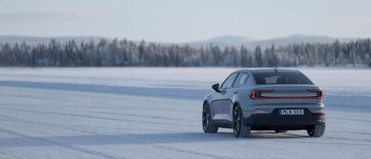 Polestar 2 en couleur Vapour, vue de biais par l’arrière, sur un champ enneigé.