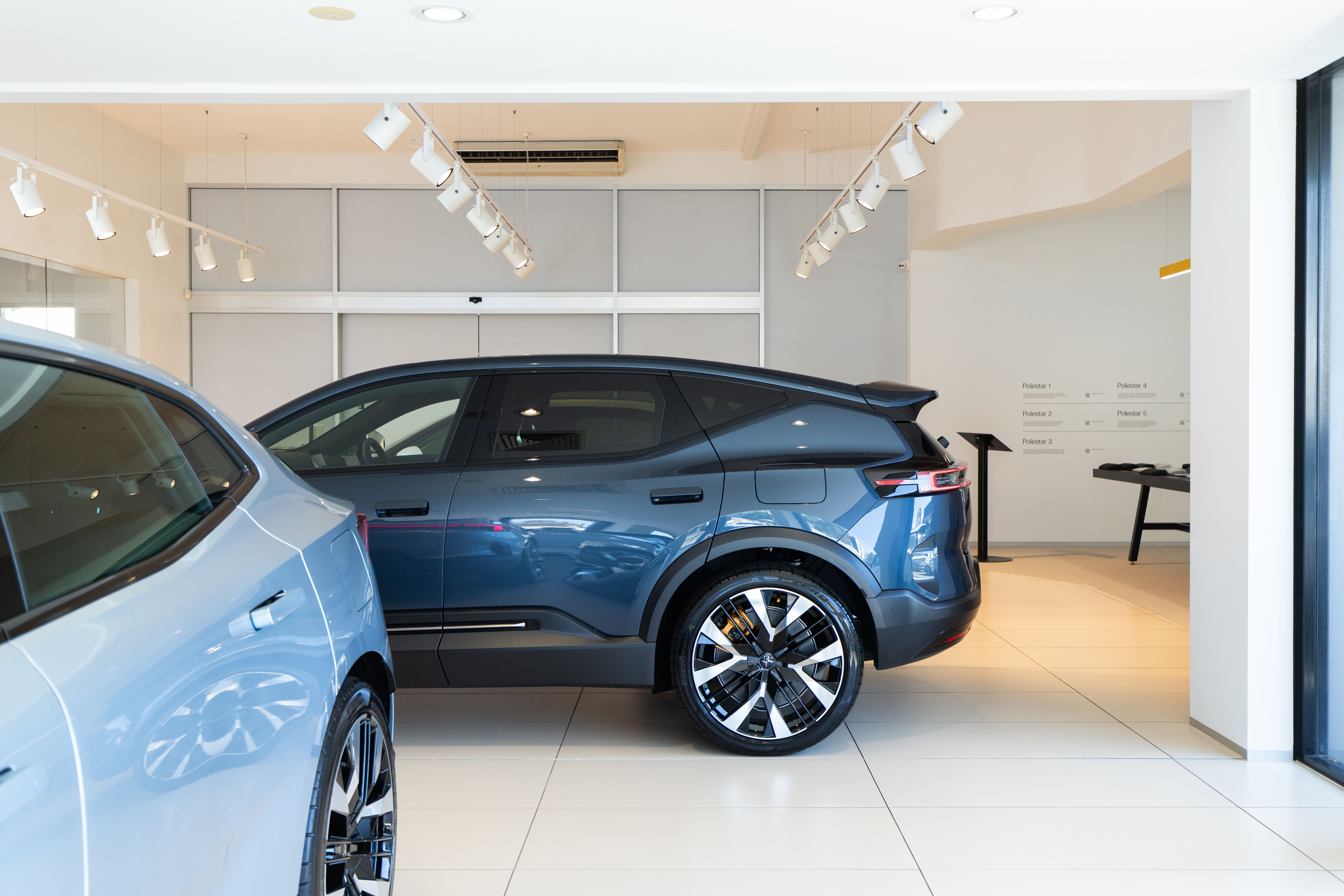 Polestar 4 side view parked perpendicular to Polestar 4 inside showroom