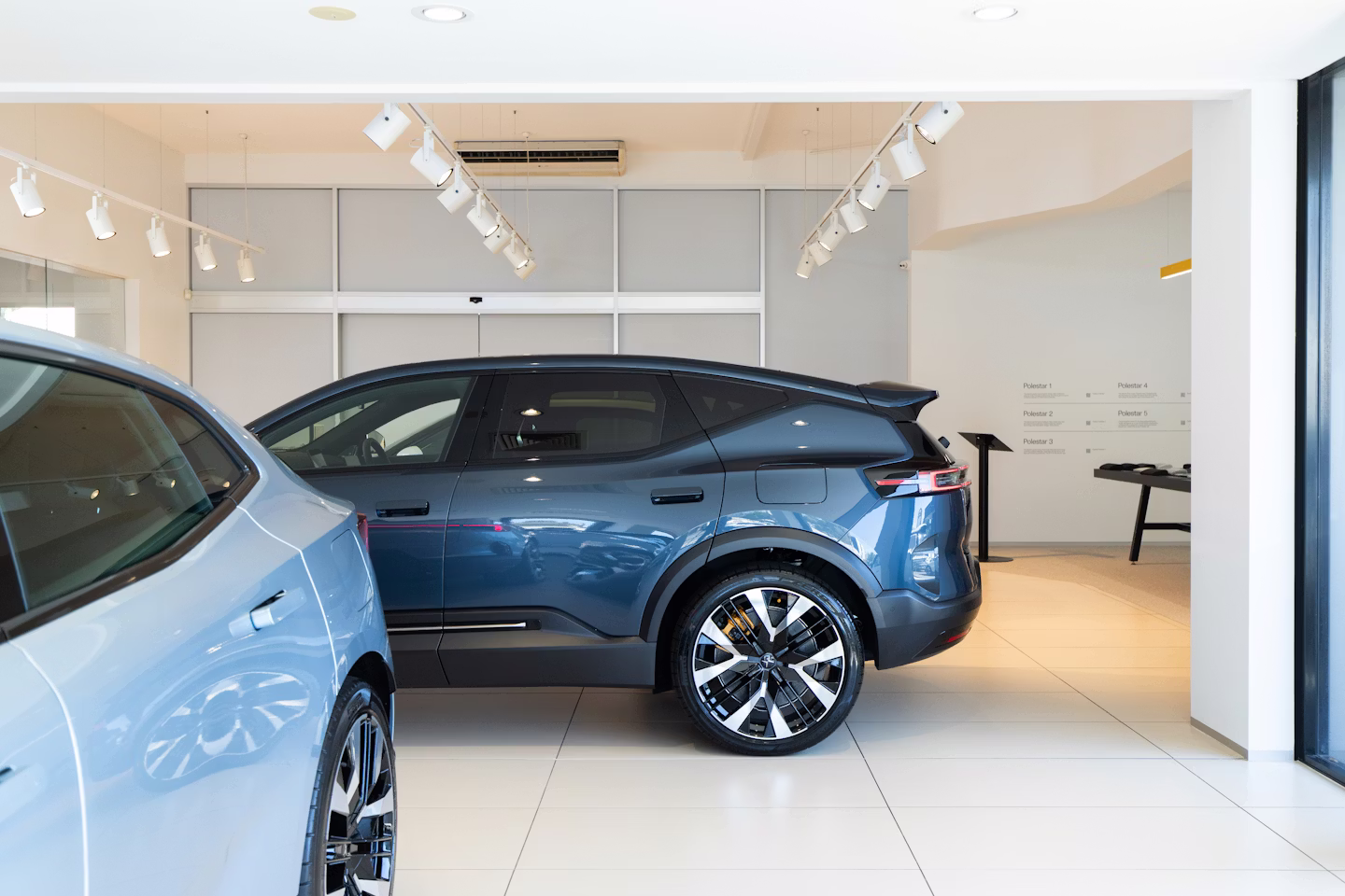Polestar 4 side view parked perpendicular to Polestar 4 inside showroom