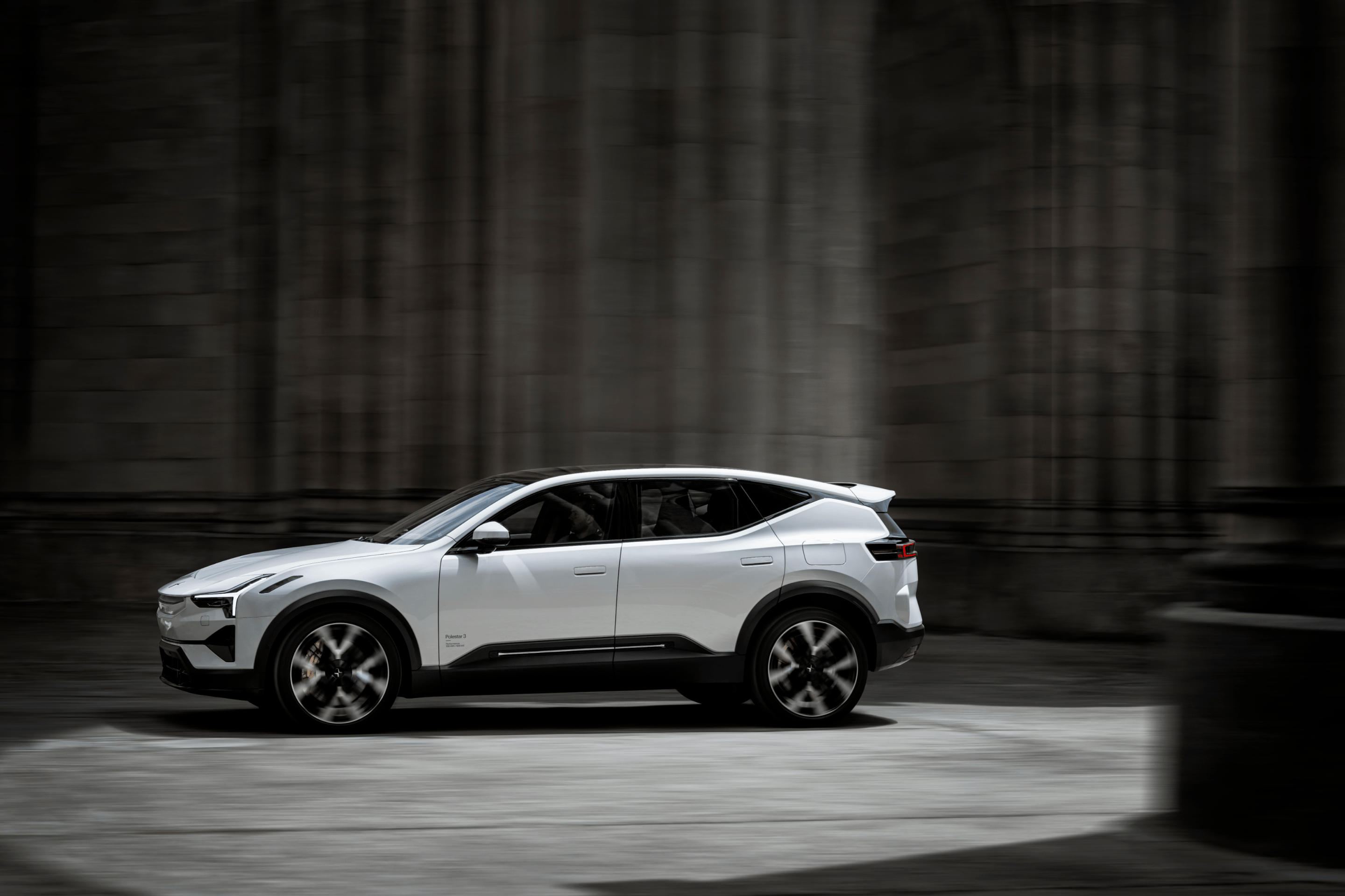 A white Polestar 3 driving between grey stone columns and walls.