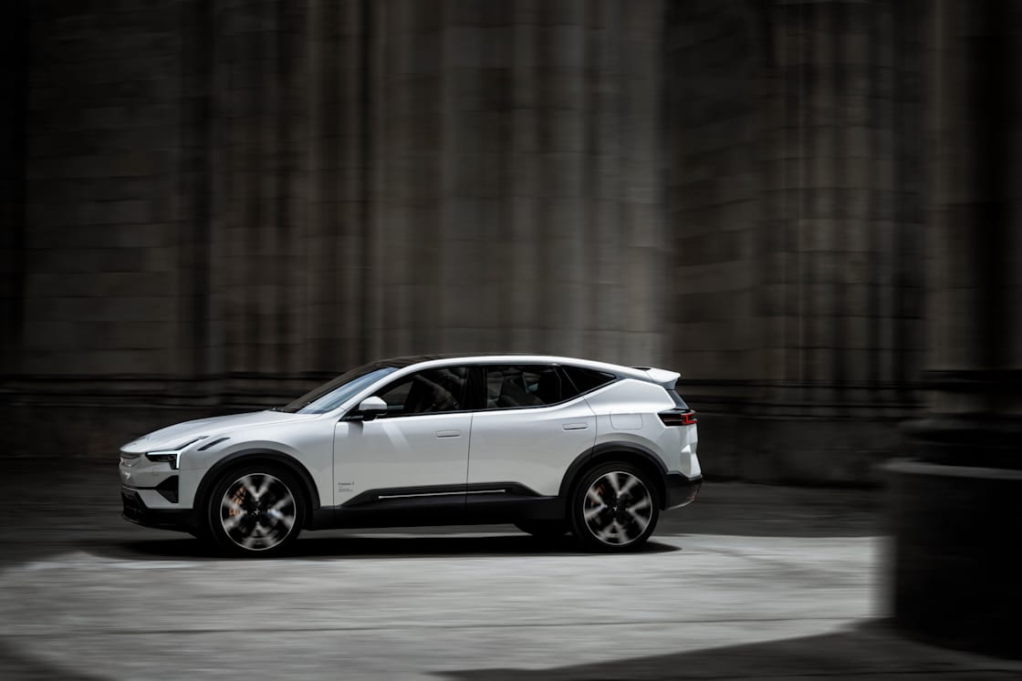 A white Polestar 3 driving between grey stone columns and walls.