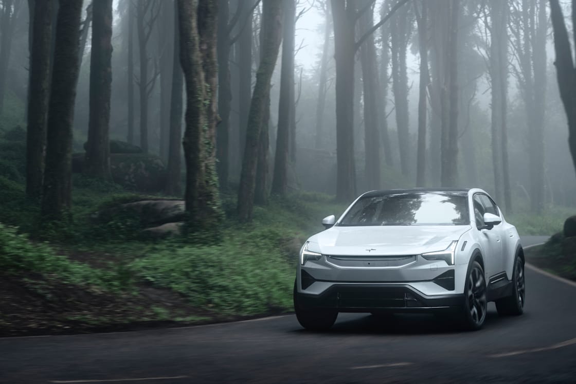 A white Polestar 3 driving on a road in a foggy environment with trees and green foliage.