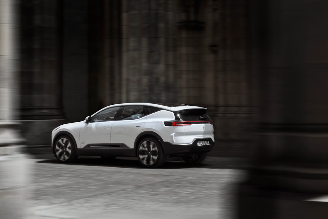 A rear-angled view of a white Polestar 3 driving between grey stone walls and columns.
