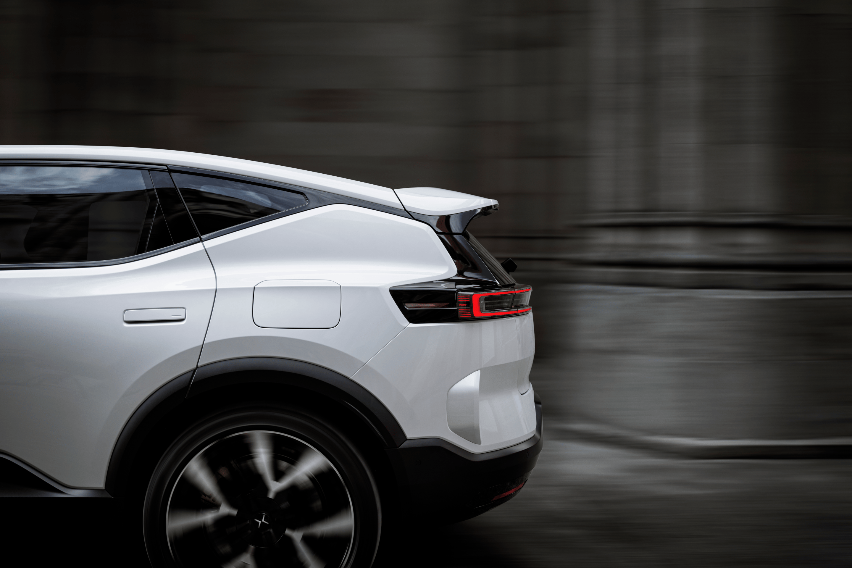 A side view of the back half of a white Polestar 3 driving by grey stone walls and columns.