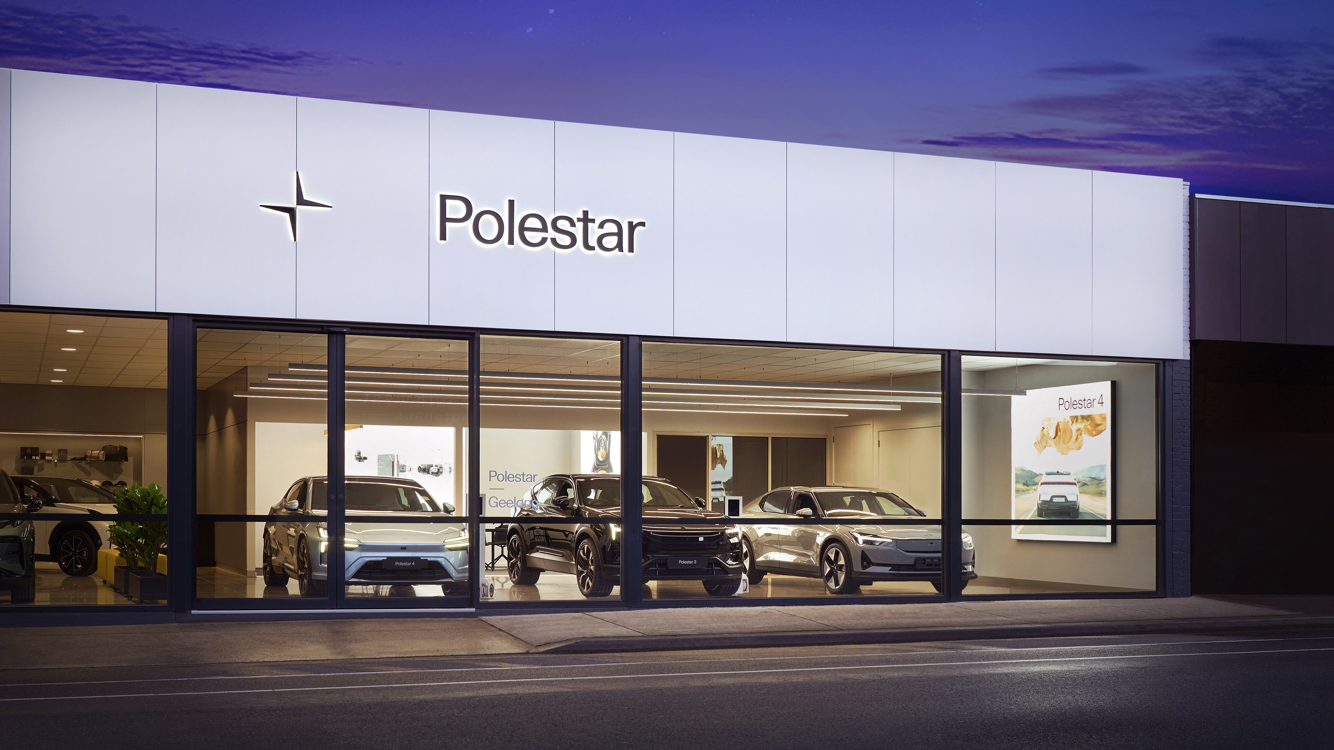 Shot of Polestar Geelong from across the road at dusk. Polestar 2, 3 and 4 lined up inside showroom, visible through floor to ceiling glass windows.