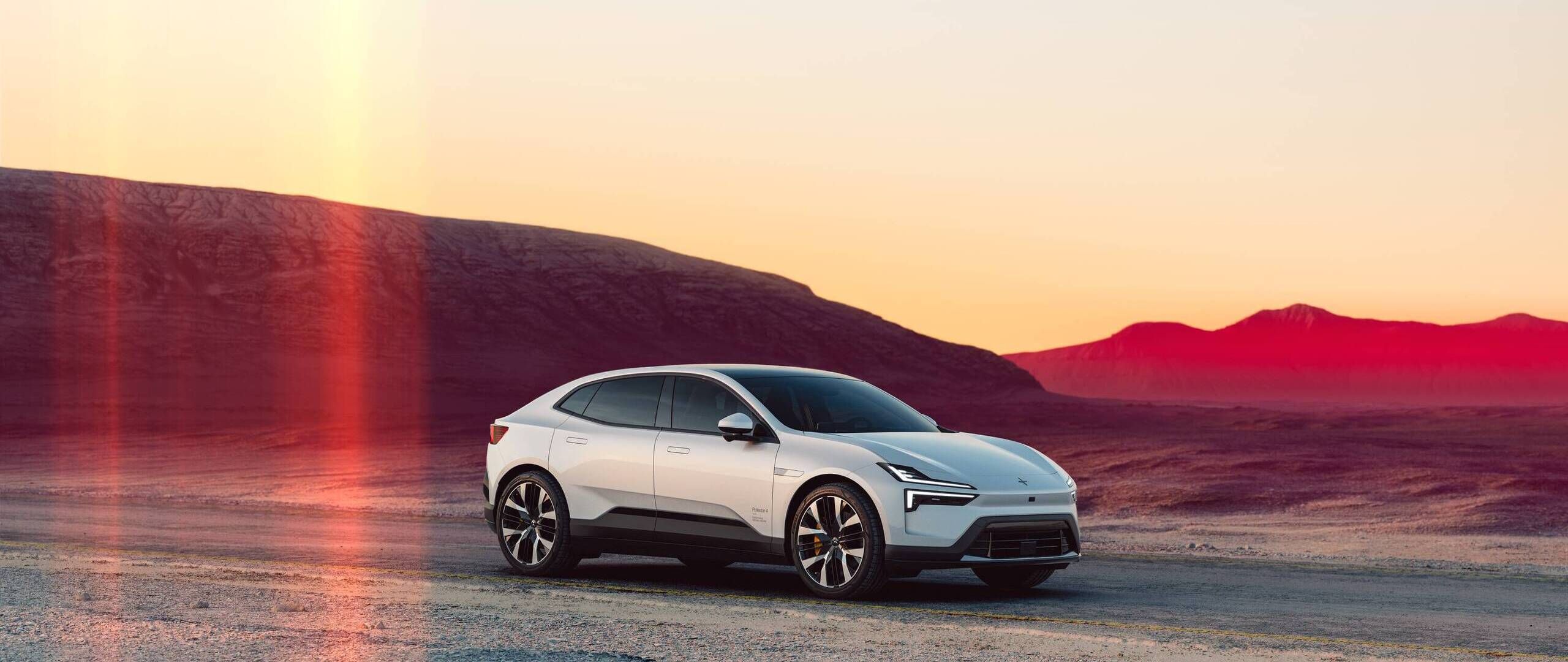 Polestar 4 in weiss schräg von vorne aufgenommen vor einer Bergkulisse bei Sonnenuntergang.