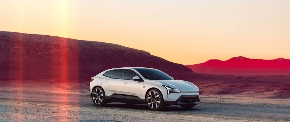 Polestar 4 in weiss schräg von vorne aufgenommen vor einer Bergkulisse bei Sonnenuntergang.