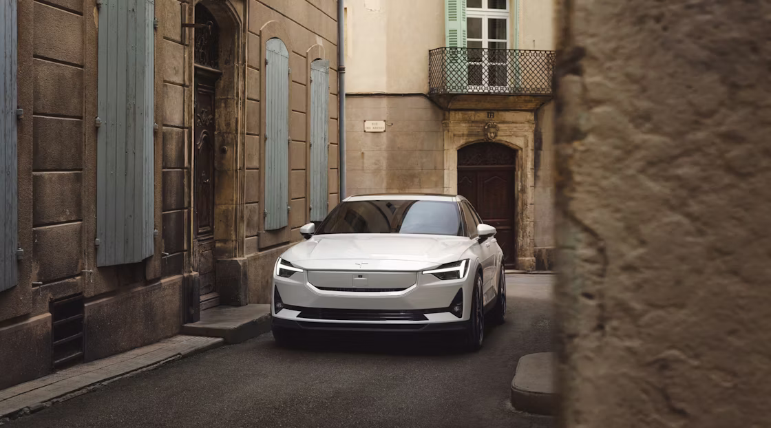 Polestar 2 in Snow colour parked in an alleyway between brown coloured buildings with blue accents.