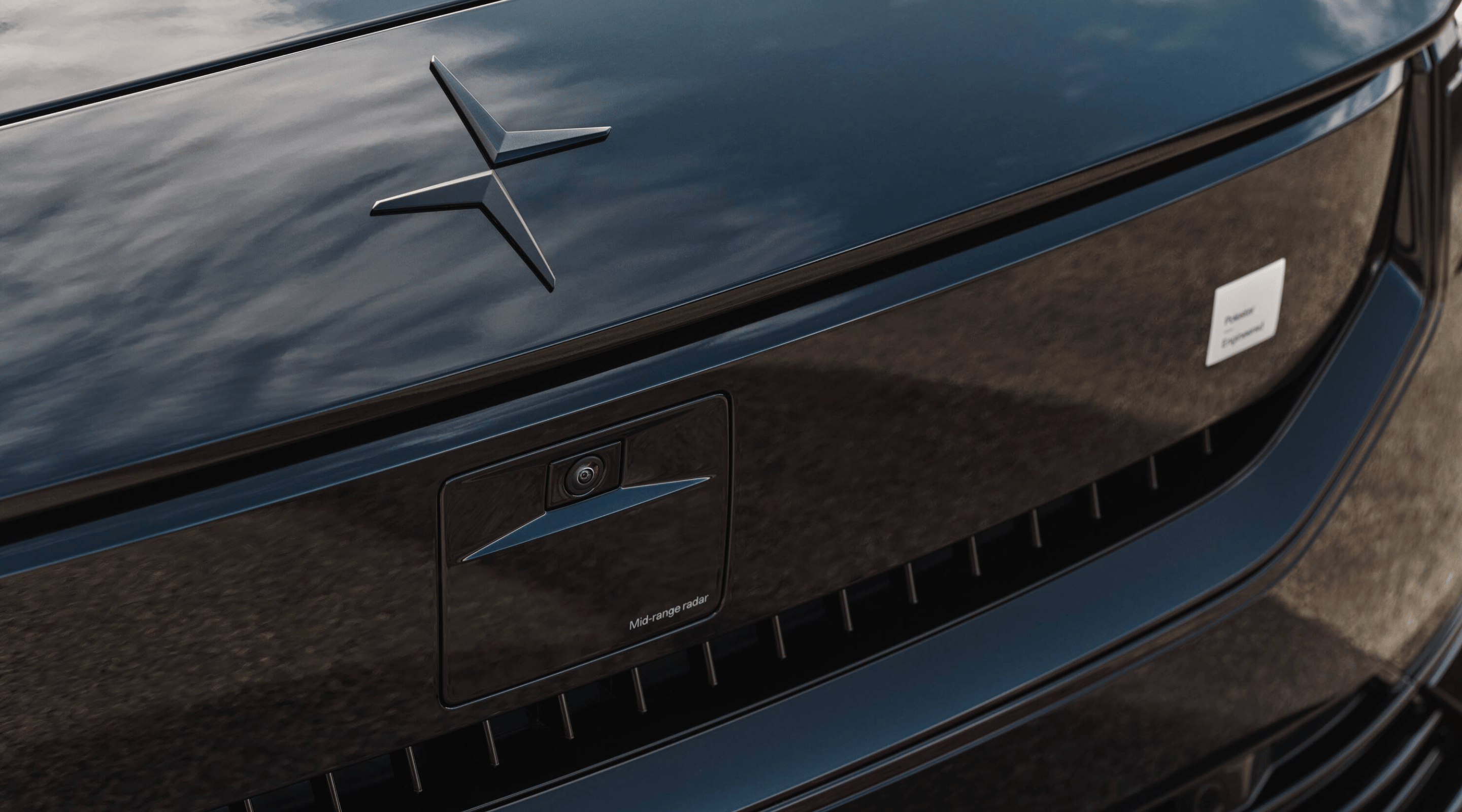 Close-up of Polestar 2’s hood with Polestar logo and smartzone with the sky reflected on surface.